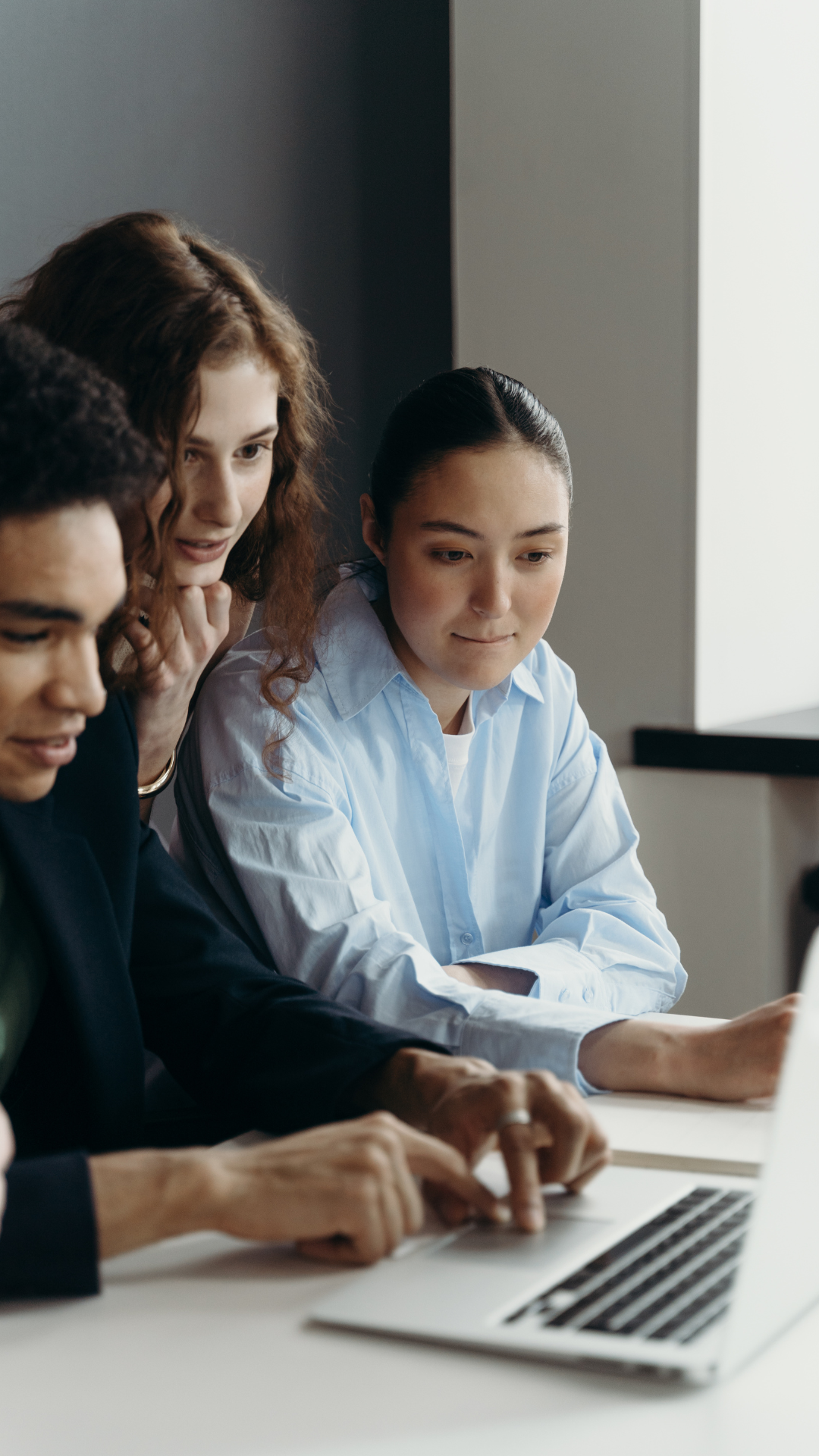 Zwei Frauen und ein Mann sitzen an einem Schreibtisch und schauen auf einen aufgeklappten Laptop.