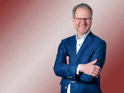 Porträt eines brünetten Mannes mit Brille und blauem Blazer.