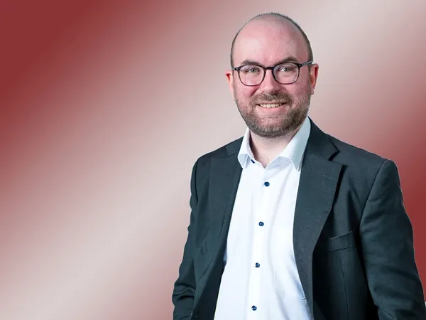 Porträt eines Mannes mit Glatze und weißem Hemd sowie Blazer.