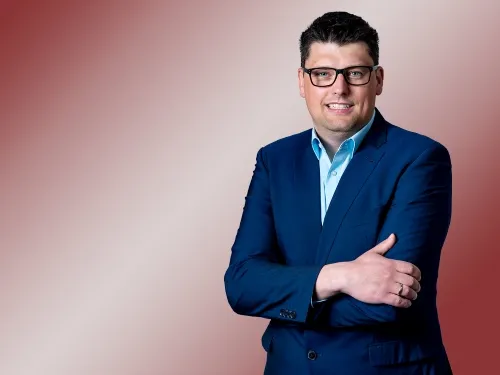 Porträt eines brünetten Mannes mit Brille und Blazer.