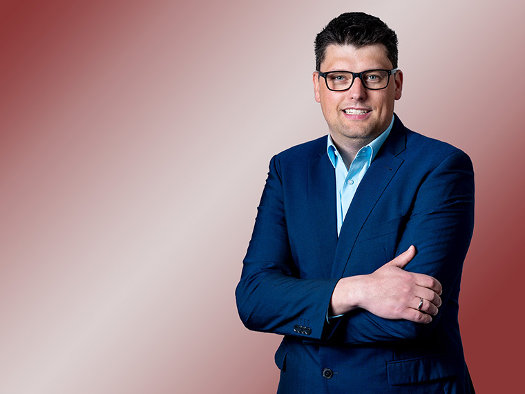 Porträt eines brünetten Mannes mit Brille und Blazer.