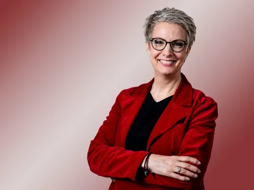 Porträt einer Frau mit Brille und rotem Blazer.