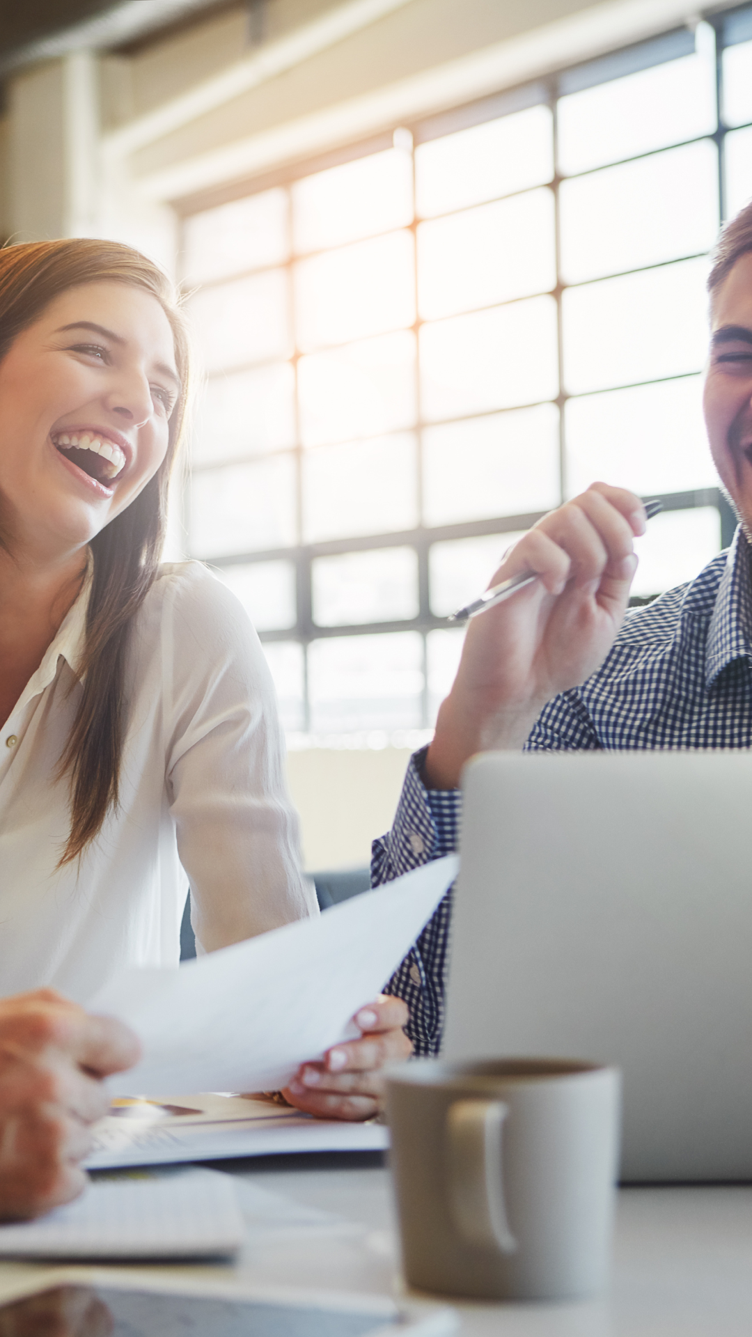Ein Mann und eine Frau sitzen lachend an einem Schreibtisch.