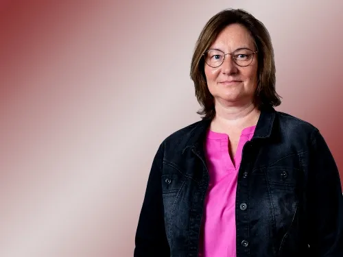 Porträt einer Frau mit Brille und pinkem Shirt sowie Jacke.
