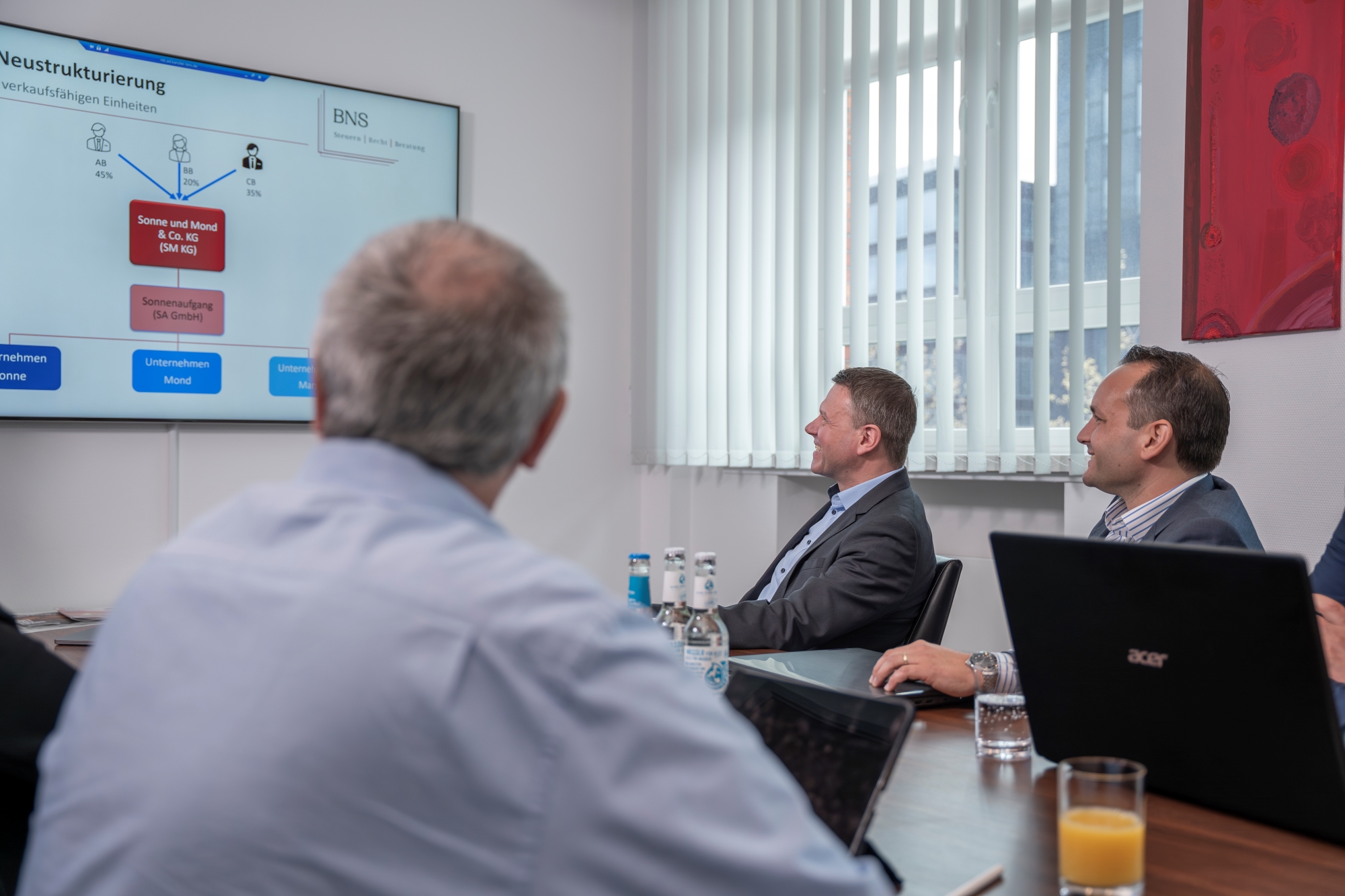 Mehrere Personen sitzen an einem Konferenztisch und schauen auf einen Bildschirm an der Wand, auf dem eine Präsentation gezeigt wird.