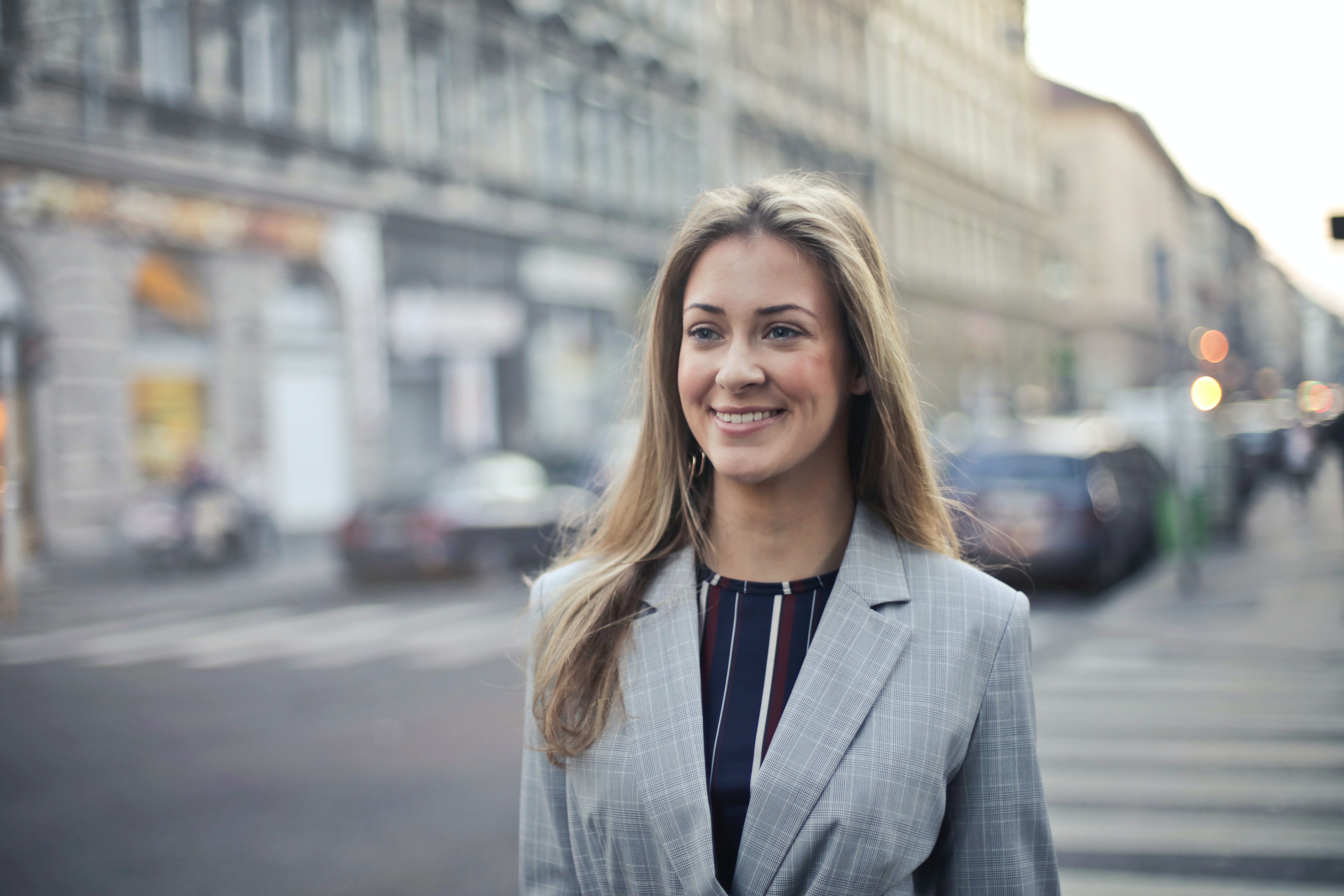 Eine blonde Frau, die einen grauen Blazer trägt, läuft lächelnd auf einer Straße.