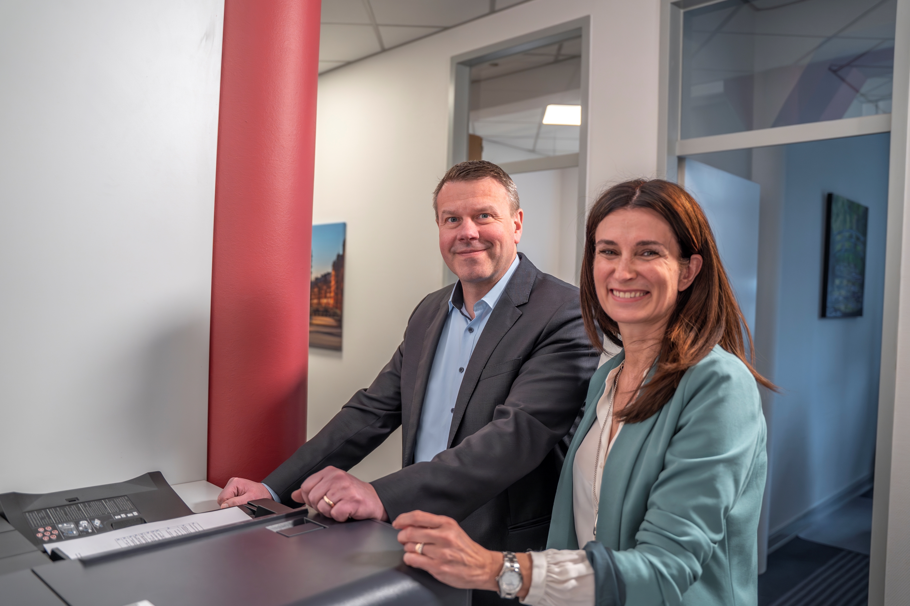 Eine Frau und ein Mann stehen an einem Tisch und lächeln in die Kamera.